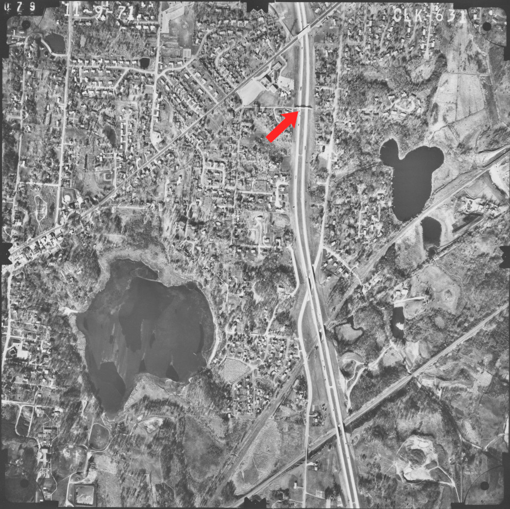An aerial black and white photo with neighborhoods and a highway visible.  A red arrow points to one of the bridges.